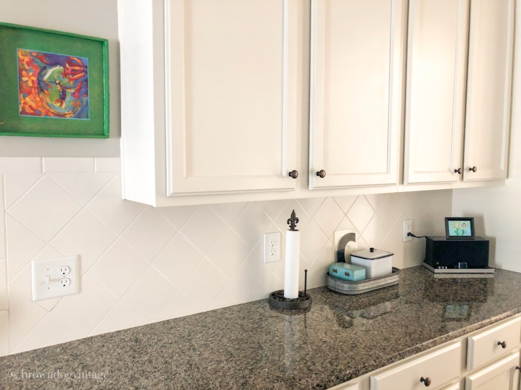 Closeup of kitchen tile backsplash surrounded by white cabinets and a dark granite countertop.