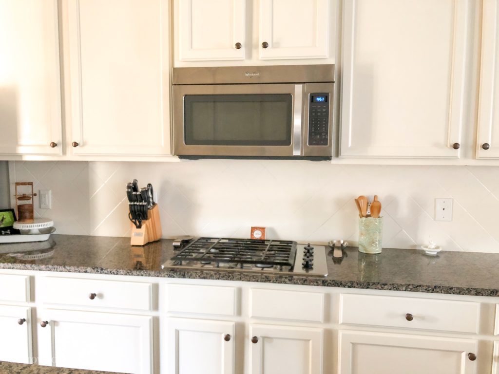 A kitchen with an over-the-oven microwave, gas range, white cabinets, and white tile backsplash.