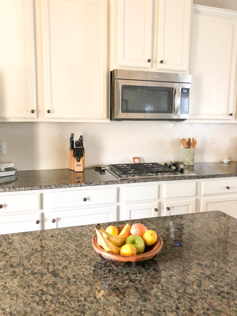 A kitchen with white cabinets, white tile backsplash, and dark granite countertops.