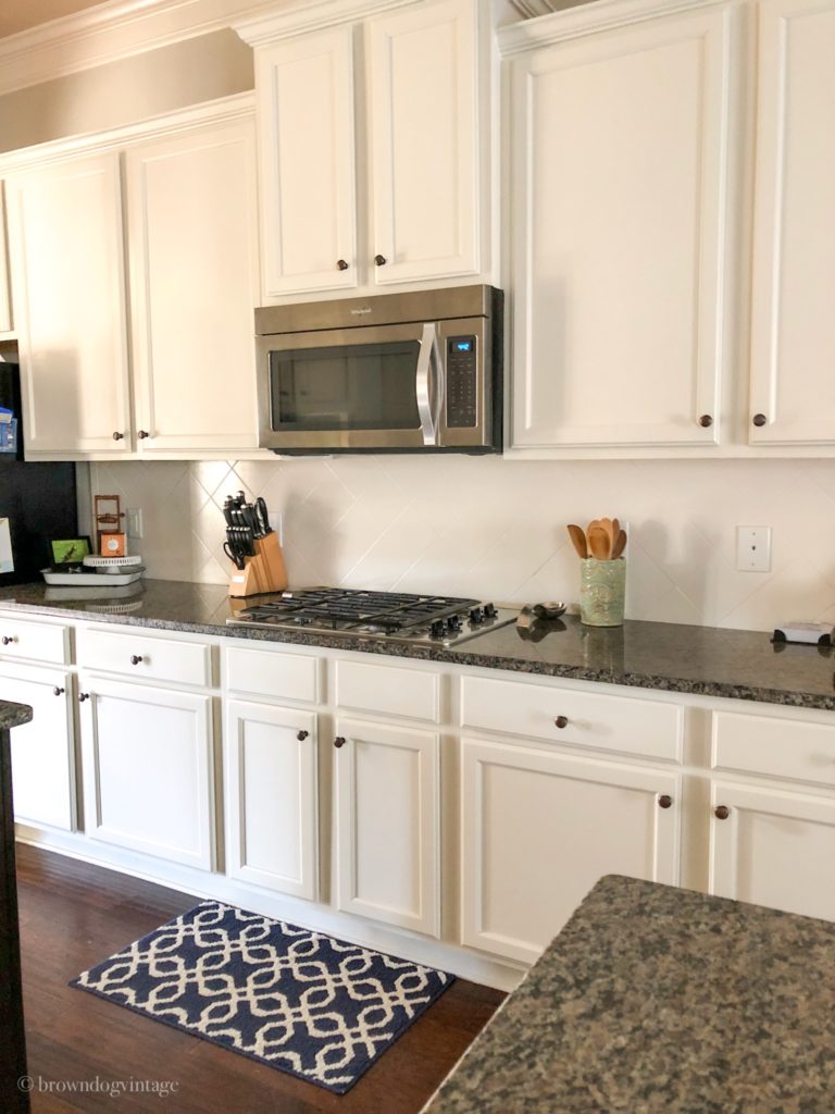 A kitchen with creamy white cabinets and diamond-shaped tile backsplash in the same color.