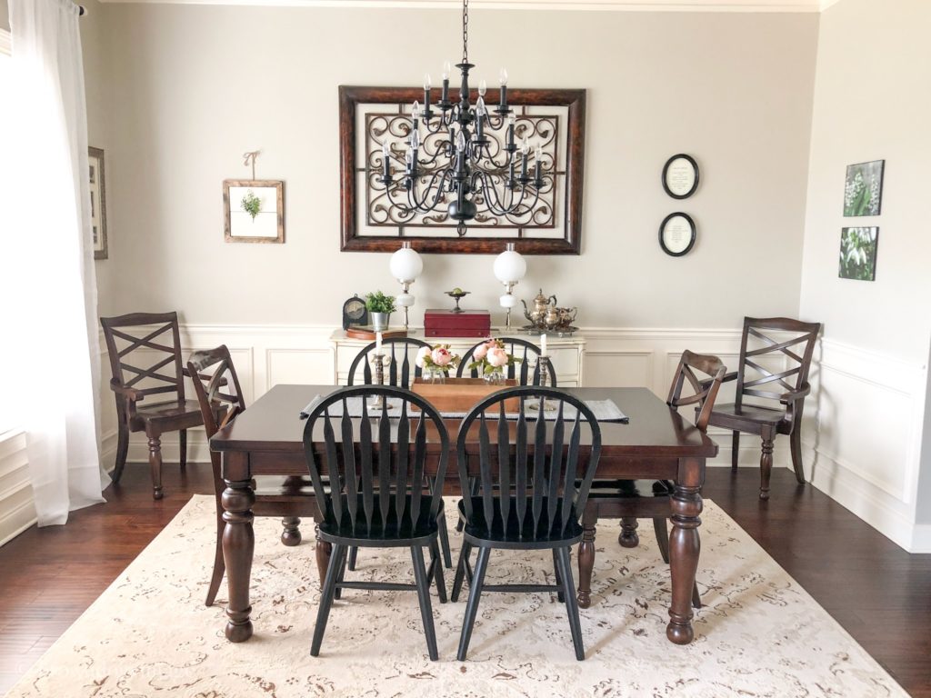 A dining room with a dark wood table, black chairs, and pink flowers on top.