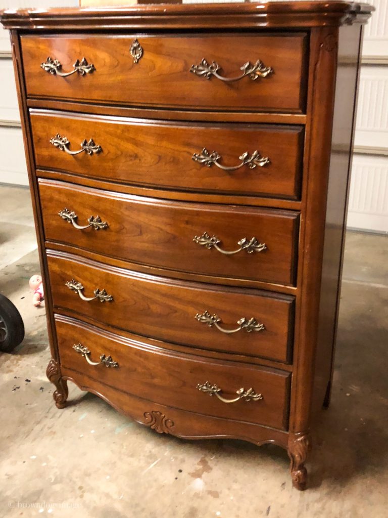 A dark brown antique dresser sits on the floor of a workshop. 