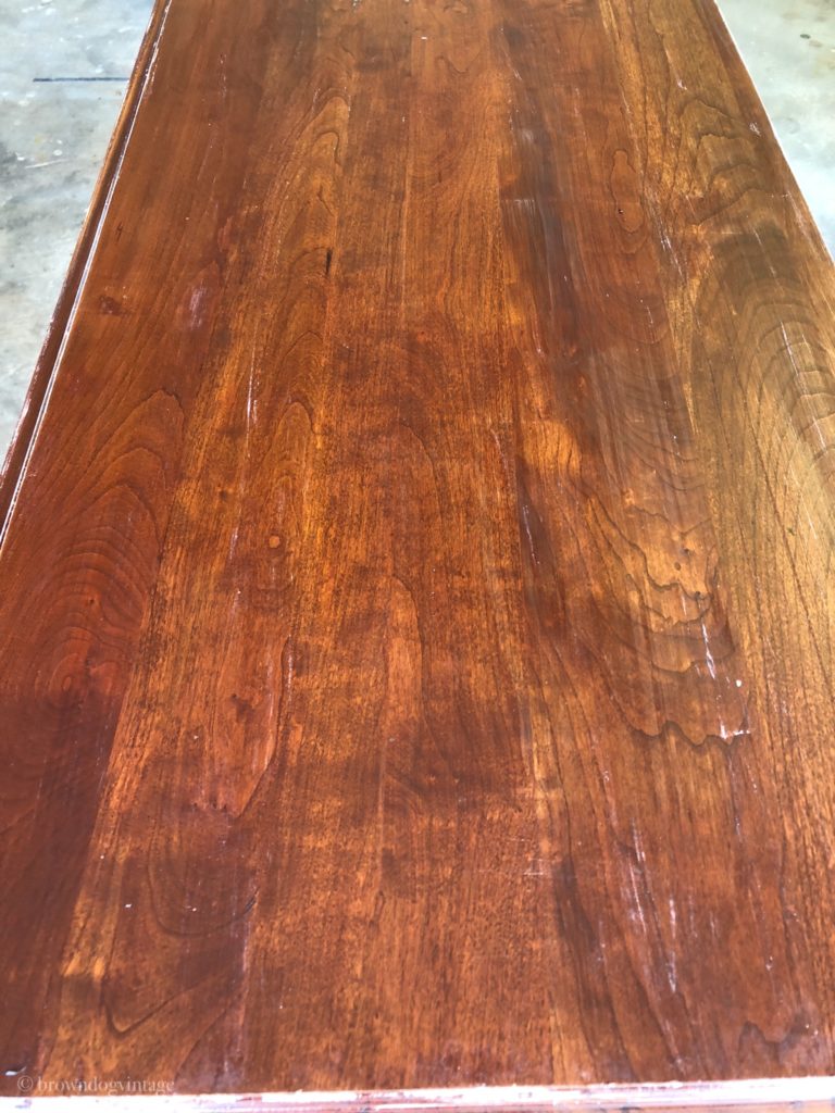 The top of a wooden buffet table with a few remaining streaks of cream paint after being stripped.