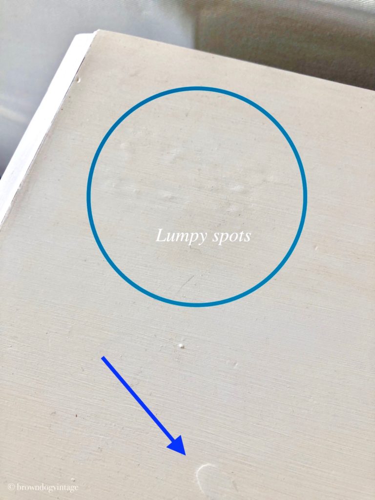 The top of a cream-colored buffet with a blue circle, arrow, and text overlay that reads \"lumpy spots\".