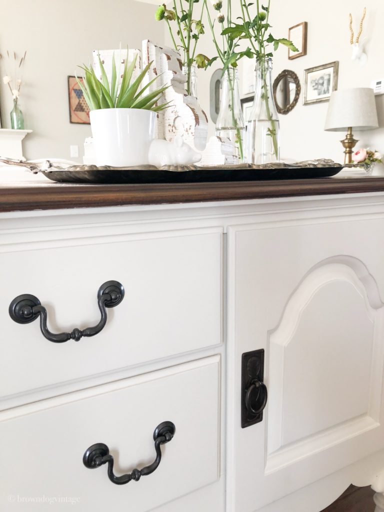 Side angle few of an antique buffet with black hardware and decor on top.