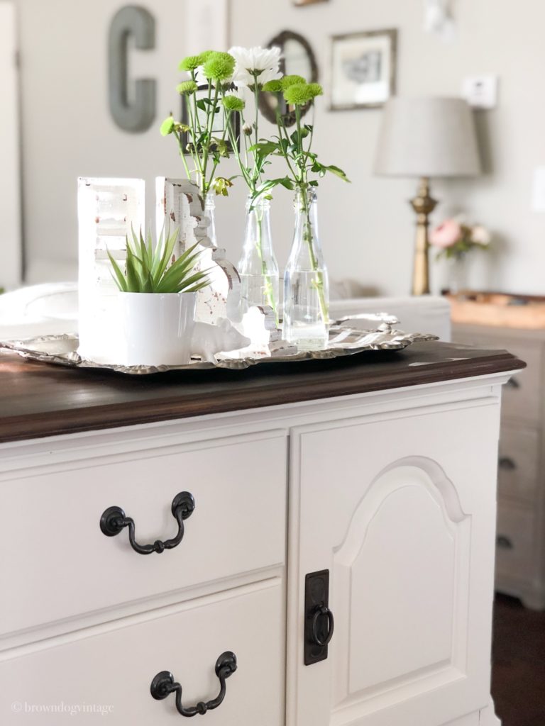 A farmhouse antique side board with green plants in a white planter and glass jars.