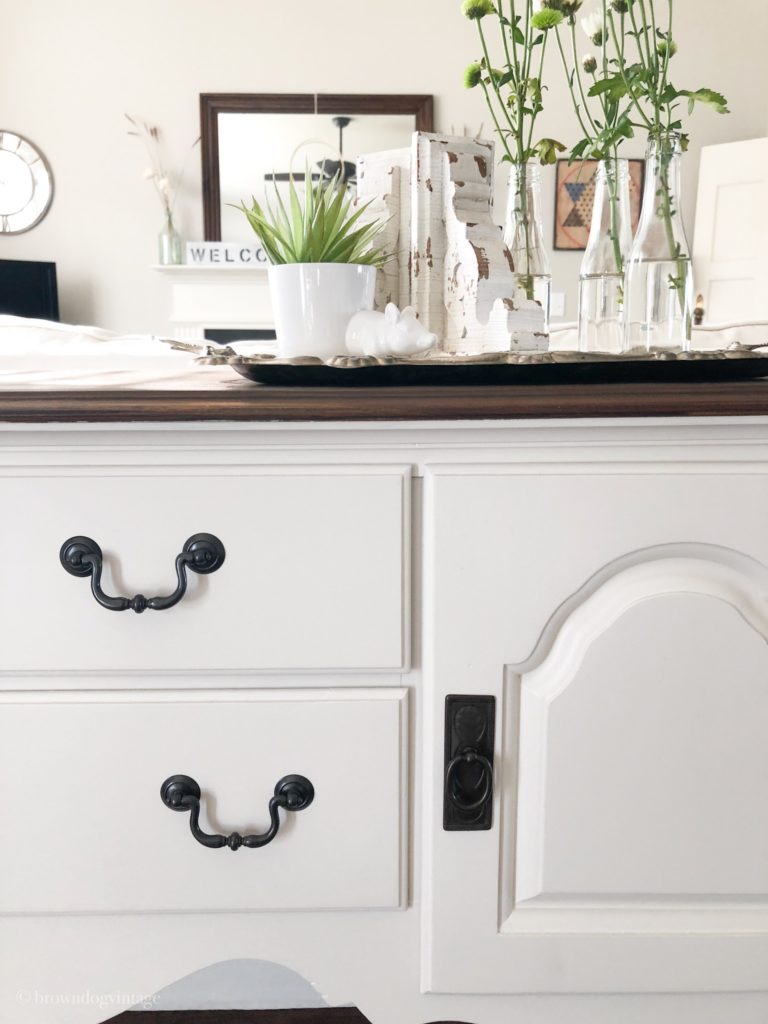 Closeup of a painted buffet table with black vintage hardware and decor on top.