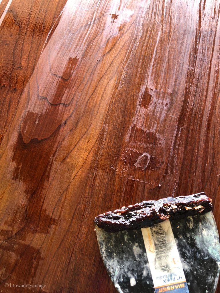 A scraper tool and the top of a wooden buffet with white streaks.