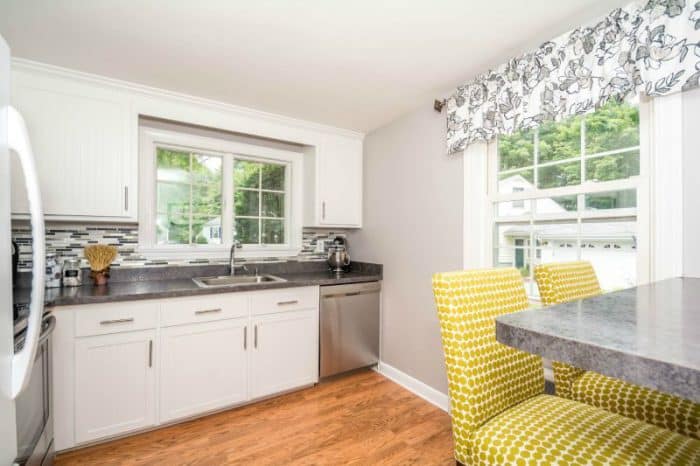 A kitchen with white cabinets, gray countertops, and a gray and white backsplash along with a dining table with yellow chairs.