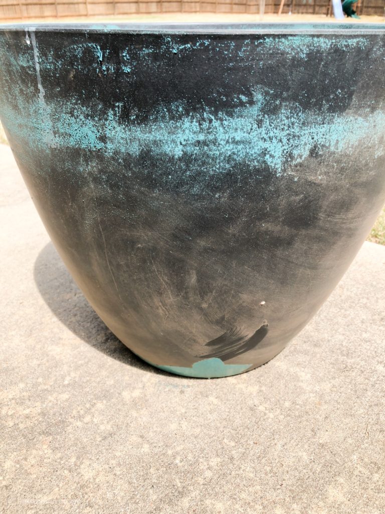 A worn teal and gray planter sits on a patio outside.