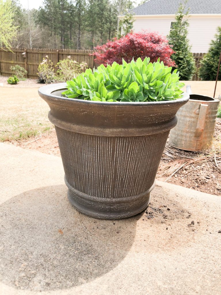 A large brown outdoor planter pot with greenery inside.