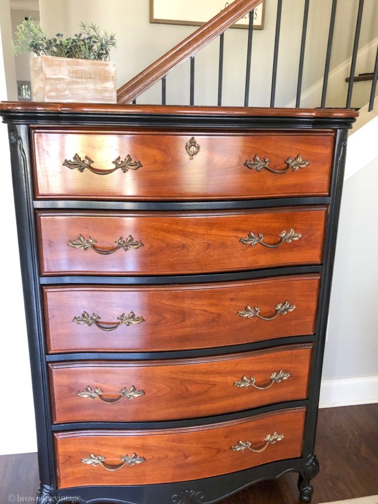 An antique dresser with black paint details in front of a staircase.