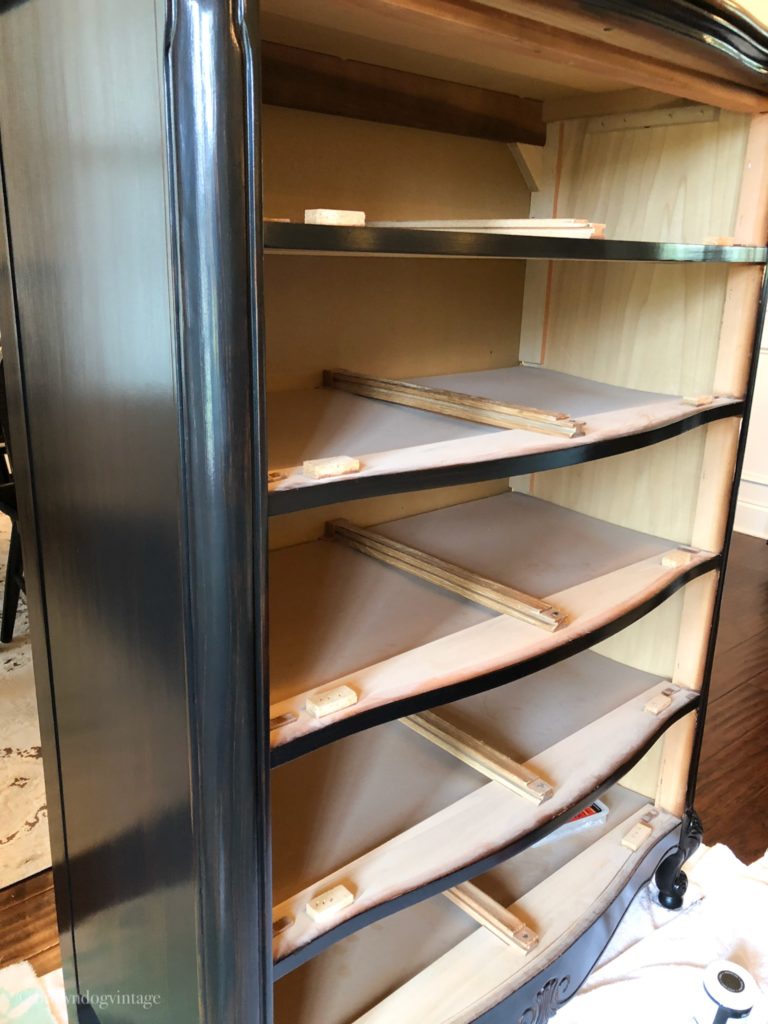 Progress shot of an antique dresser being painted black in a workshop.