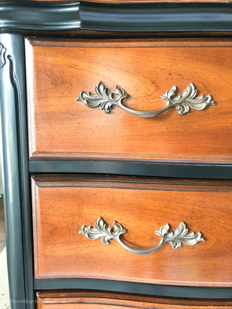 A dark wood dresser with black paint details and ornate silver pulls.