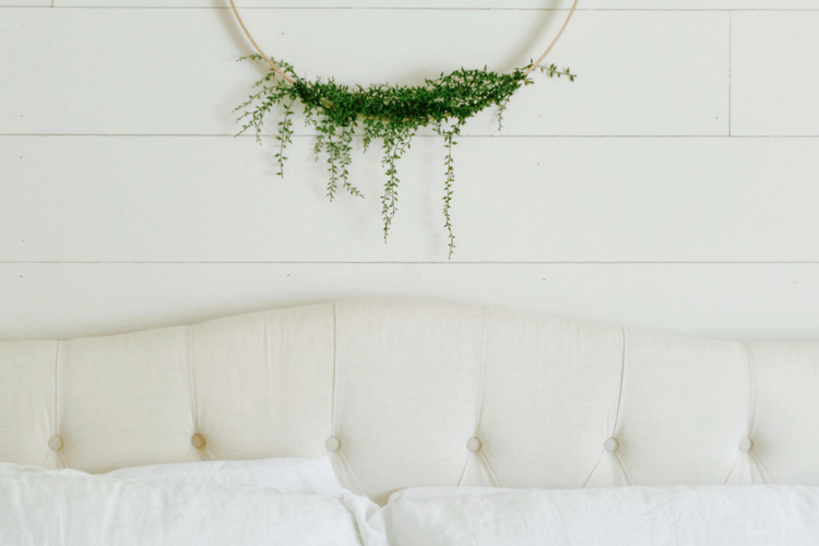 White shiplap bedroom wall with a bed and hoop wreath with greenery.