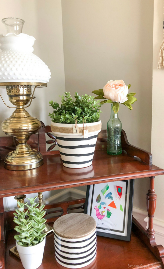 A painted terra cotta planter with green plants inside on an antique side table with a brass lamp.