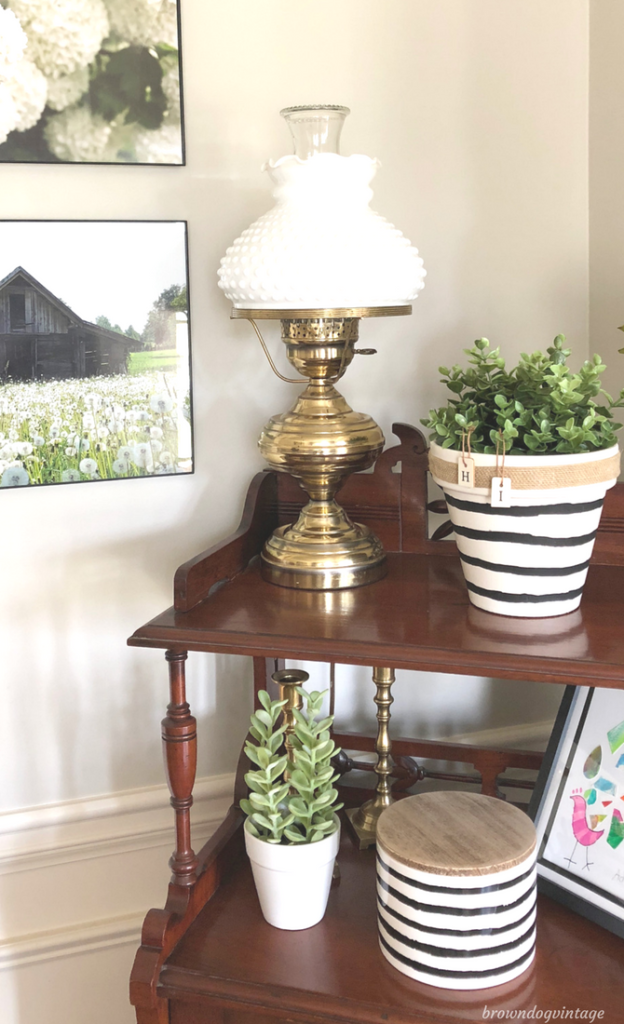 A white and black striped potted plant on a side table with a brass lamp and decor.