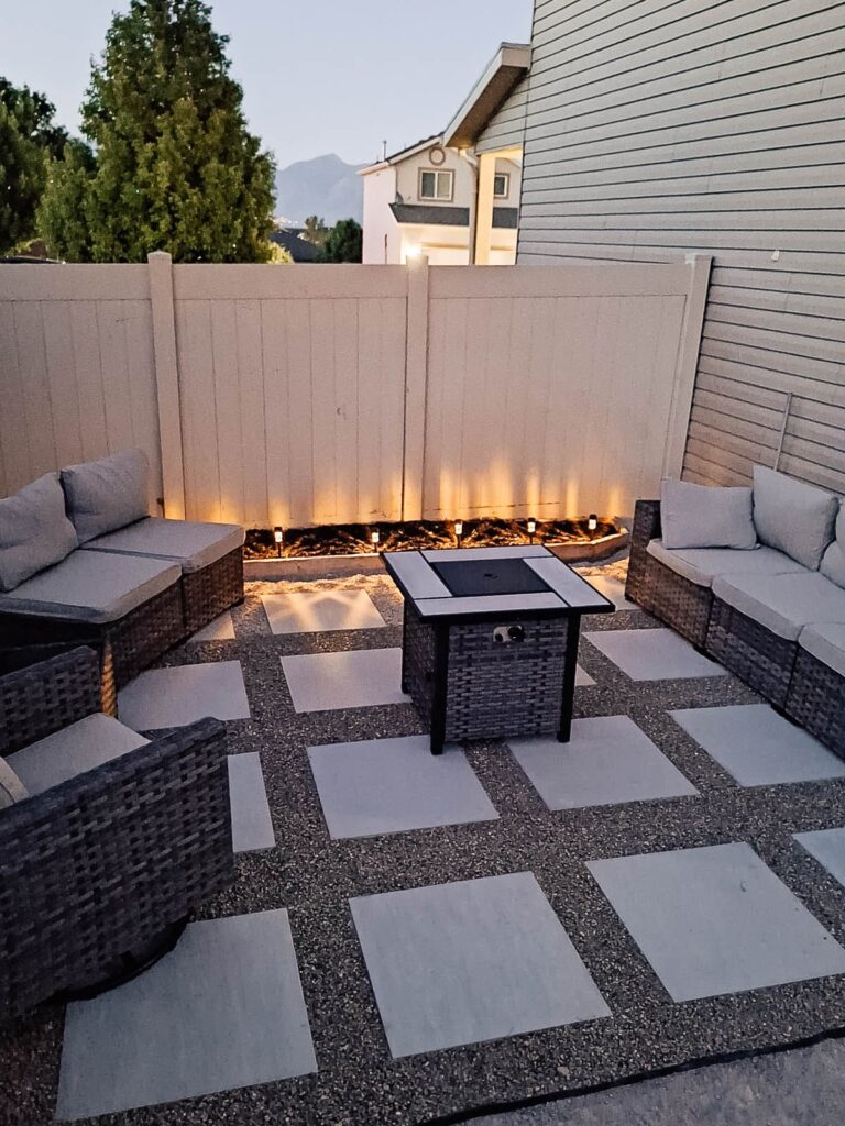 Paver patio fire pit area on the side of the house with outdoor furniture and solar lights.