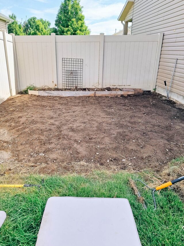 A dugout dirt area on the side of a house in the corner of a fence.