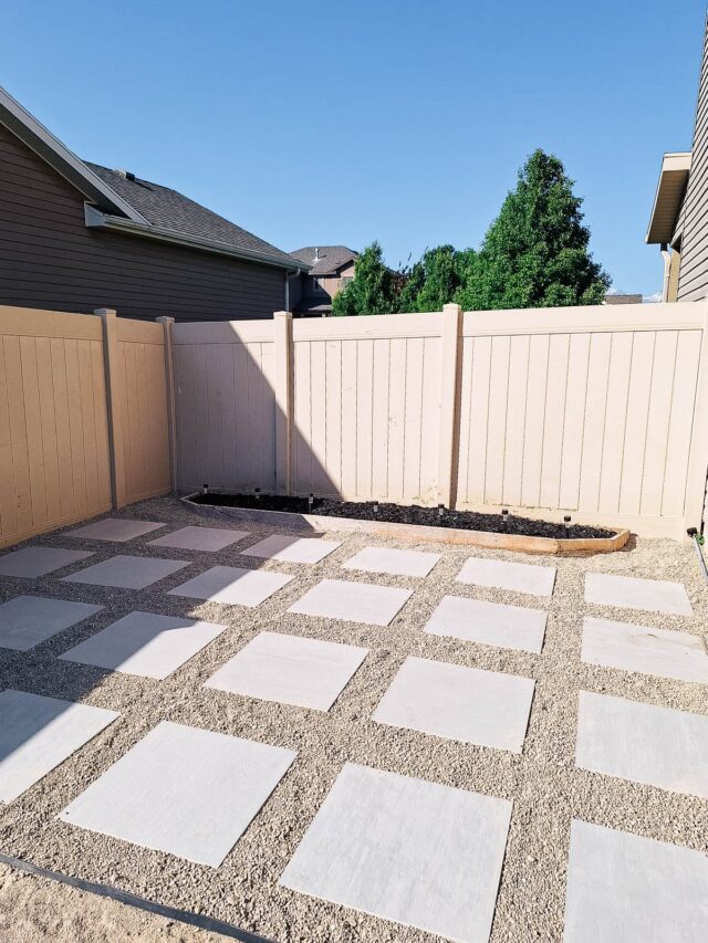 Freshly laid paver patio with gravel in the fenced area on the side of a house.