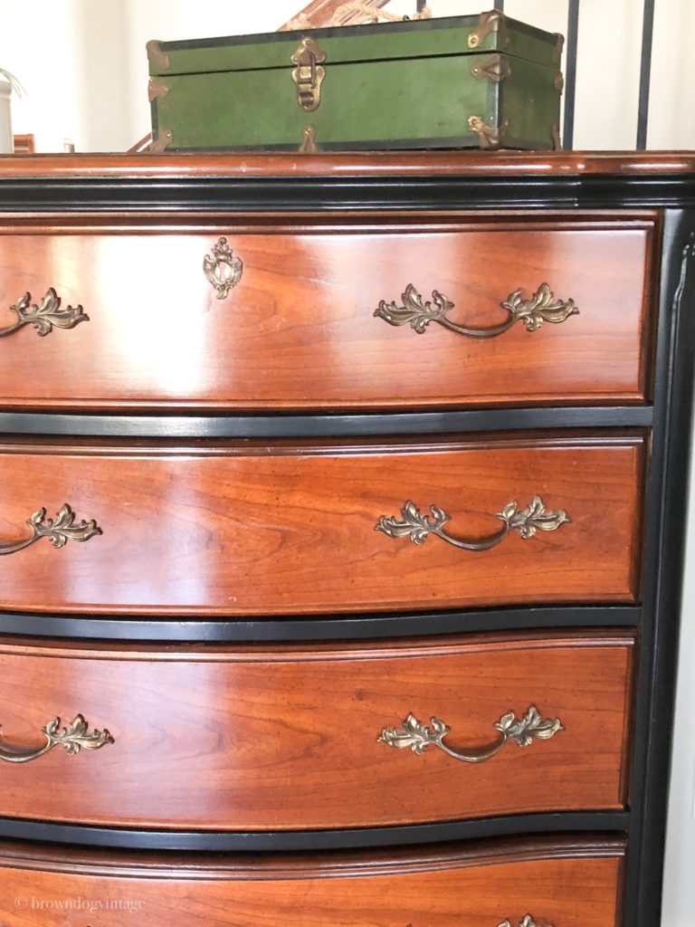 A wooden dresser with black details and ornate silver handles.