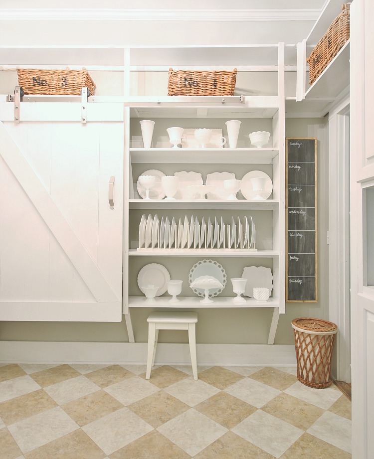 A farmhouse style barn door in a pantry filled with white plates and cups.