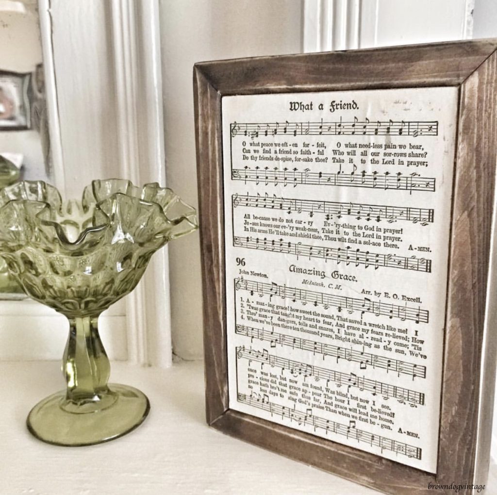 Sheet music in a rustic wooden frame next to an antique green glass vase.