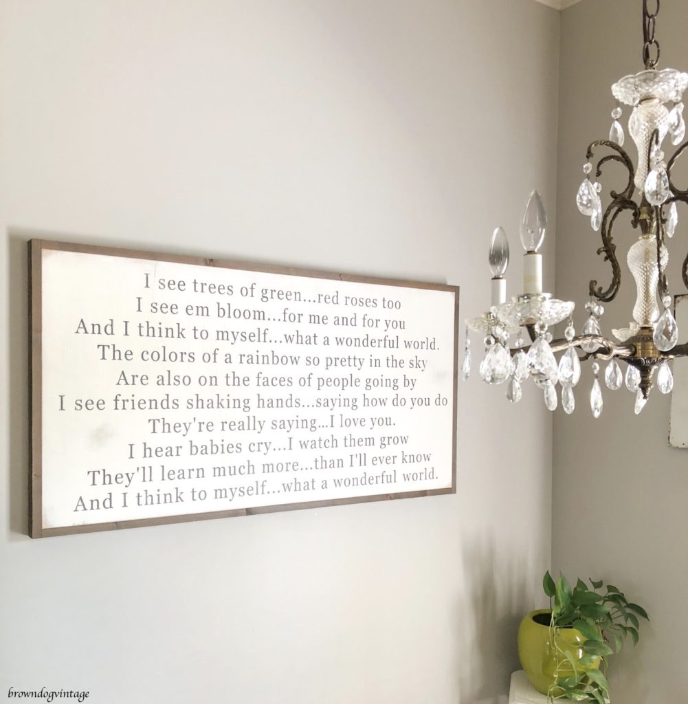 A large rectangular farmhouse-style sign with black printed text and a wooden frame on the wall of a dining room.