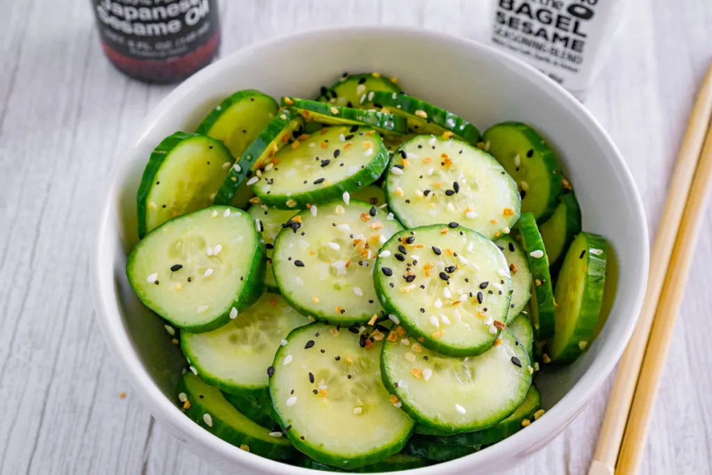 Cucumber salad with everything bagel seasoning in a white bowl next to chopsticks.