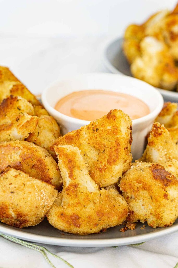 Crispy breaded cauliflower bites on a plate with an orange dipping sauce.