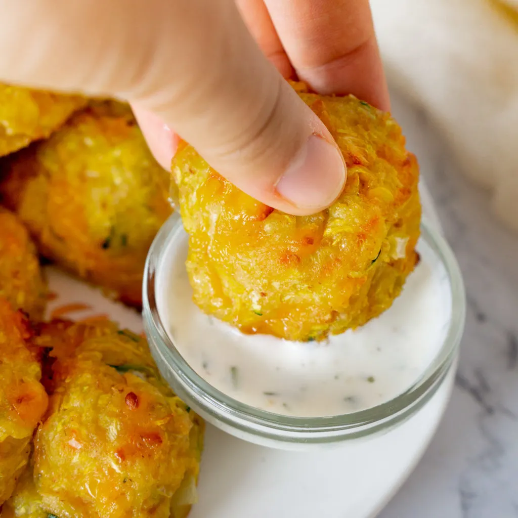 Homemade squash tots on a plate and being dunked into a small bowl of dipping sauce.