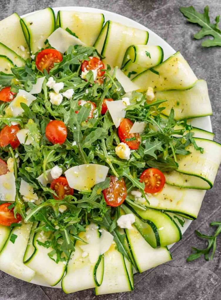 Zucchini carpaccio salad with tomatoes and shaved cheese on top.