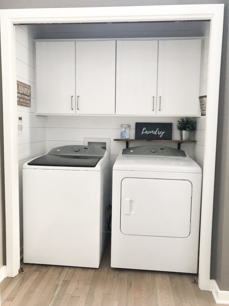 Farmhouse style shiplap walls in a laundry room with a washer and dryer and white cabinets.