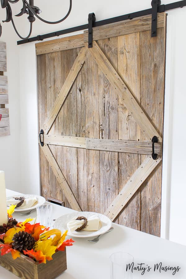 A weathered farmhouse style barn door behind a dining room table decorated with fall leaves.