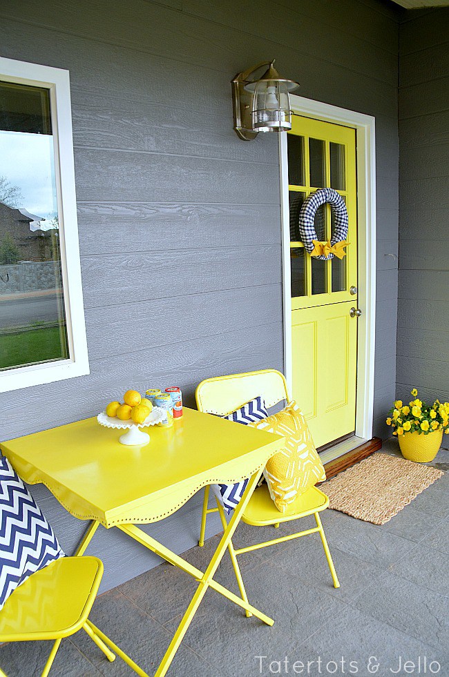 A porch with a bright yellow Dutch-style door and a yellow table and chairs with chevron pillows.