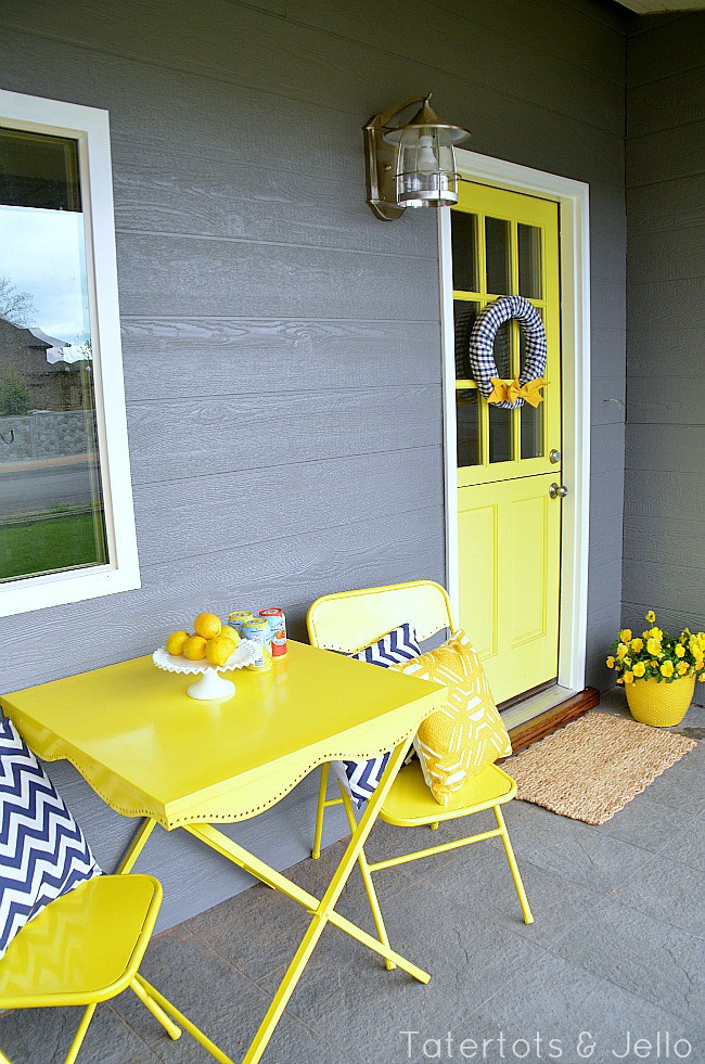 A porch with a bright yellow Dutch-style door and a yellow table and chairs with chevron pillows.