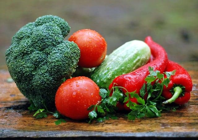 An assortment of wet vegetables, including broccoli, tomatoes, and cucumber on a wooden surface outside.