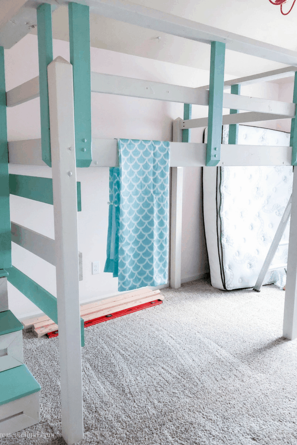 The frame of a DIY loft bed painted teal and white.