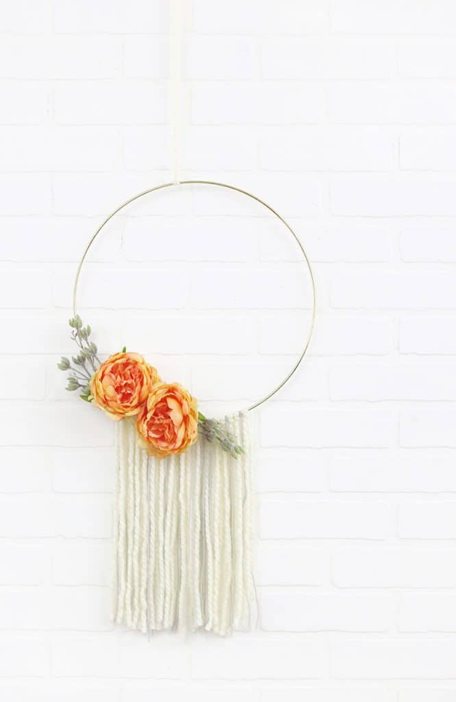 A metal hoop wreath with orange flowers and tassels hanging from the bottom.