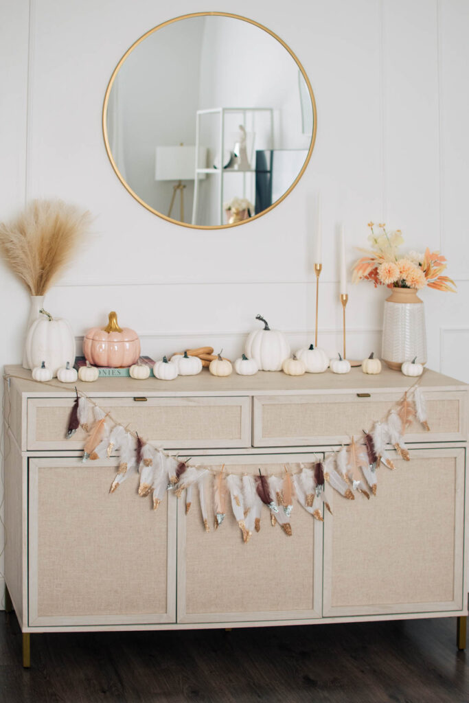 A boho feather garland for fall decor on a side table in a living room.