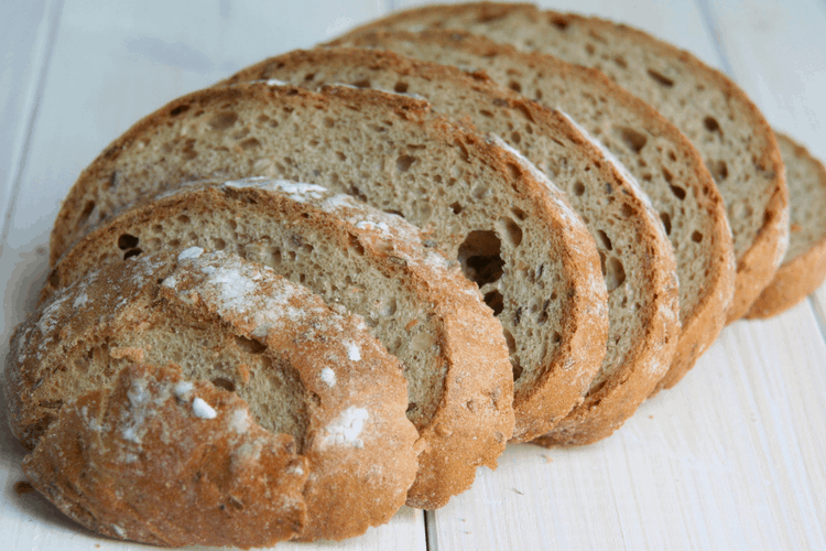 Closeup of sliced bread with white powder sprinkled on top of a white wood surface.