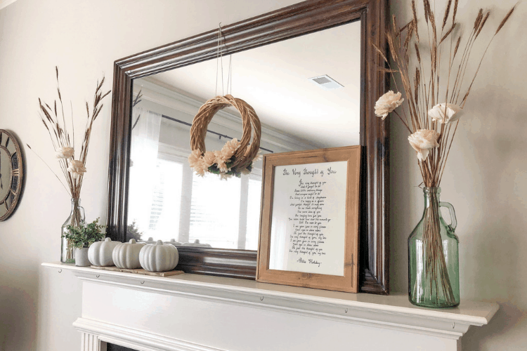 Rustic fall decor on a fireplace mantle including pumpkins, a wreath, and flowers in a glass vase.