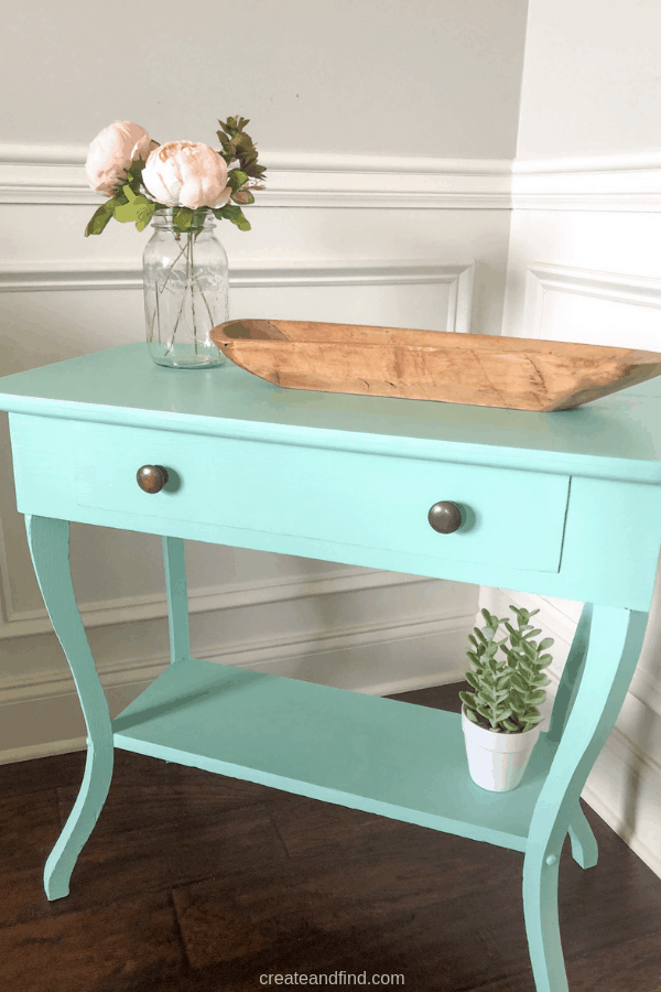 A teal side table with decor in the corner of a room.