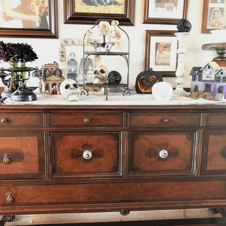 Halloween decorations on a wooden antique sideboard, including skulls, a jack-o-lantern, and haunted houses.