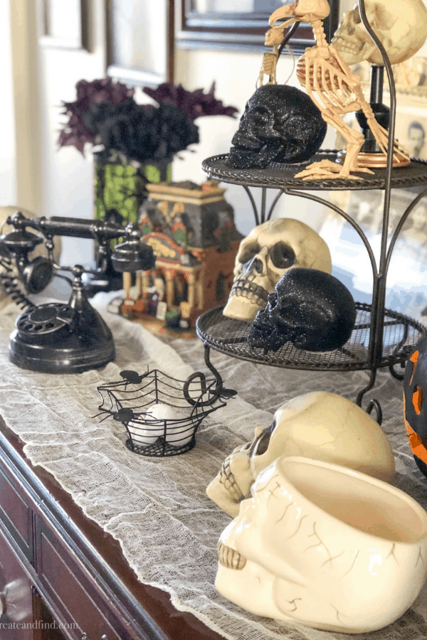 Fake white and black skulls, a miniature haunted house, and spooky decor on a side table.