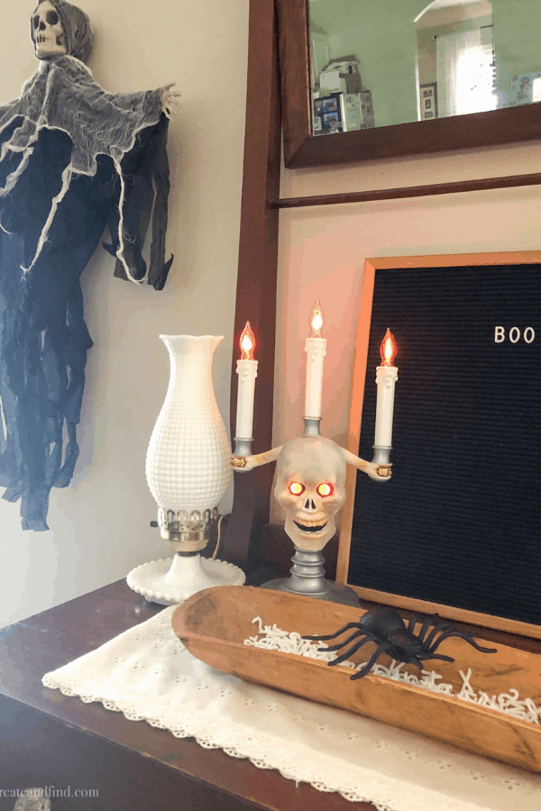 A creepy skeleton candelabra next to a black sign that says \"boo\" and a skeleton wall hanging.