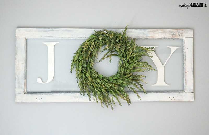 A sign with the letters \"J\" and \"y\" on either side of a green wreath to spell the word \"joy\".