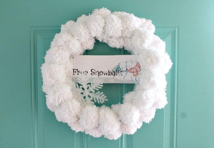 A snowball wreath on a teal front door made from pom poms.