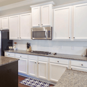 A kitchen with white cabinets and granite countertops with a dark island.