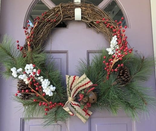 A Christmas wreath with holly and a red and green striped ribbon.